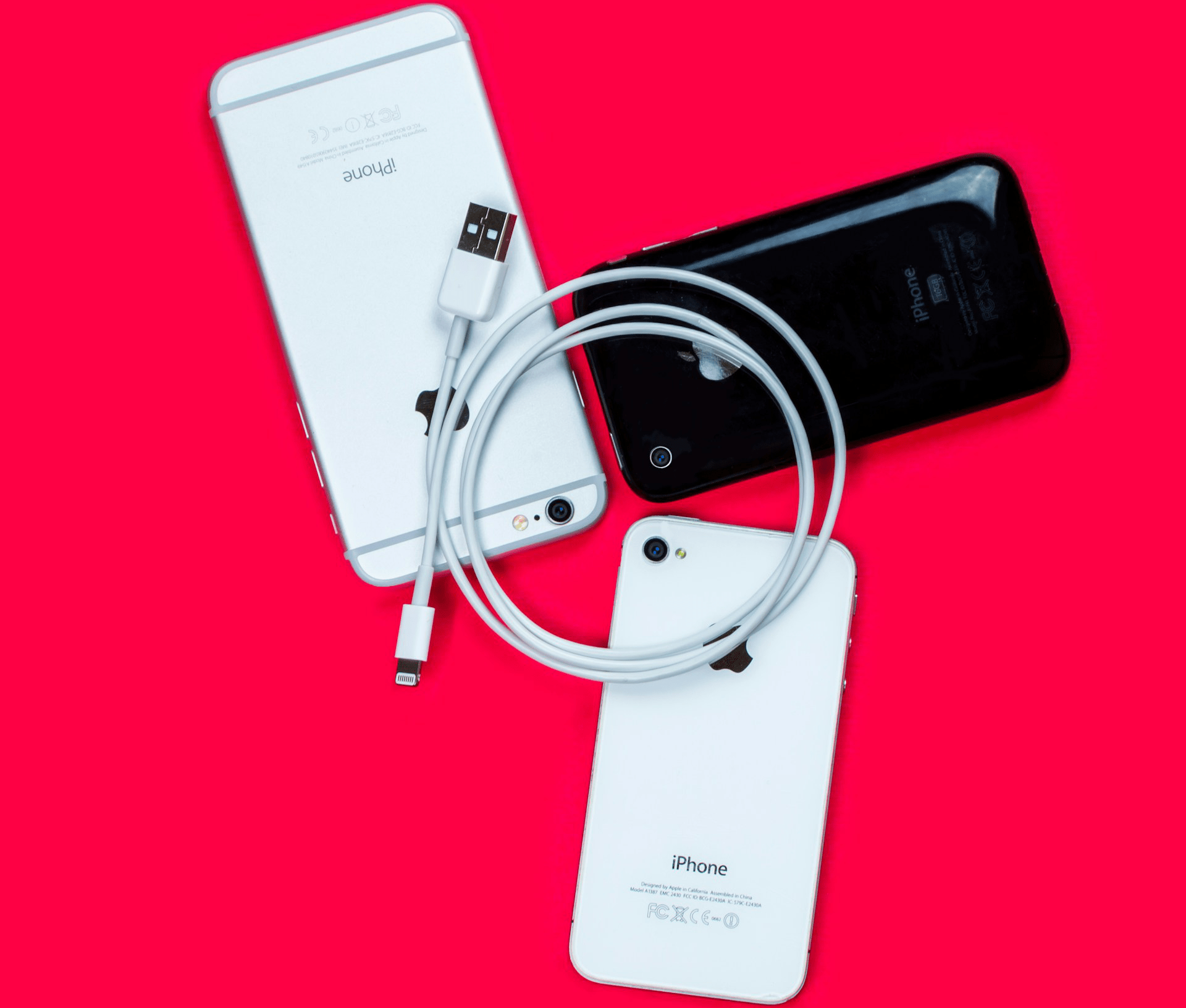 Tre ældre iPhones og et Lightning-kabel.